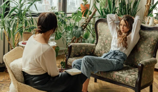 Uma paciente mulher numa sessão de terapia. Ela está sentada num sofá e com os braços estendidos.